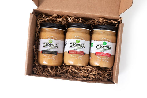 Three jars of Georgia Gourmet peanut butter in a cardboard box on a white background