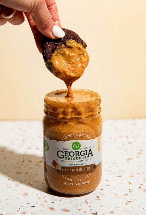 Jar of Georgia Grinders hazelnut butter with a spoonful being taken out, on a light background.
