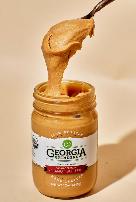 Jar of Georgia Grinders peanut butter with a spoonful being lifted out, on a beige background