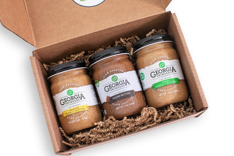 Three jars of Georgia Hummus in a cardboard box on a white background