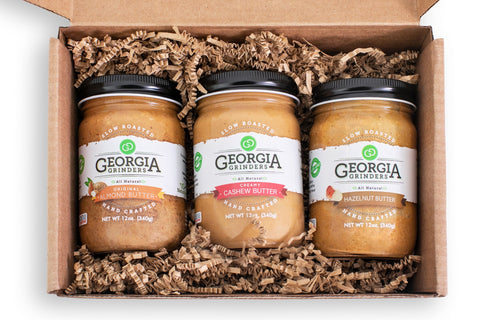 Three jars of Georgia Grinders cashew butter in a cardboard box with shredded paper.