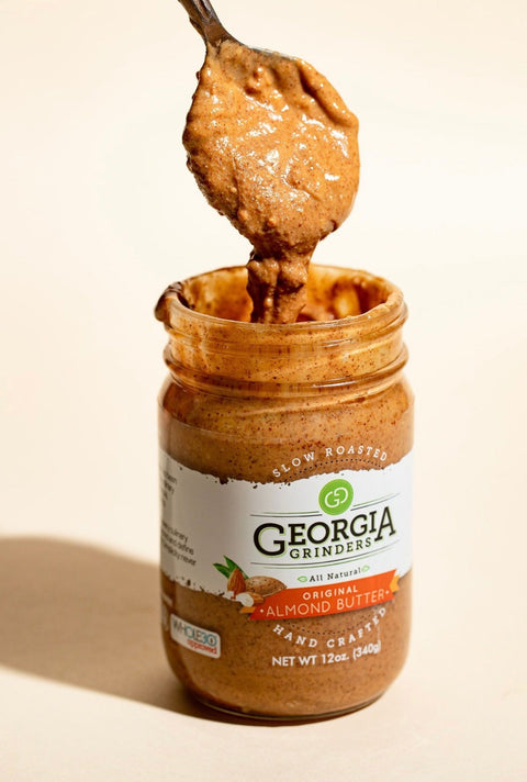 Jar of Georgia Grinders almond butter with a spoonful on top, on a beige background