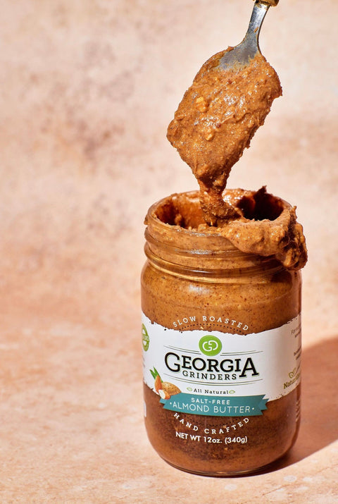 Jar of Georgia Grinders almond butter with a spoonful of butter on a beige background